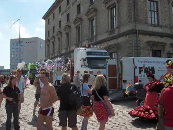 Ældre paradevogn med blokvogn og deltagere i fjerkostumer på en brostensbelagt plads i København.