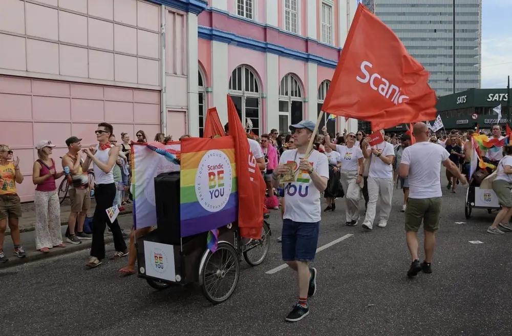 Ladcykel med regnbuefarvet banner undervejs i Copenhagen Pride-optoget, omgivet af deltagere med flag.